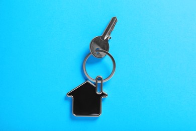 Photo of Key with trinket in shape of house on blue background, top view. Real estate agent services