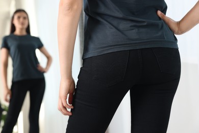 Woman in stylish black jeans near mirror indoors, closeup