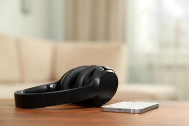 Photo of Modern wireless headphones and smartphone on wooden table indoors