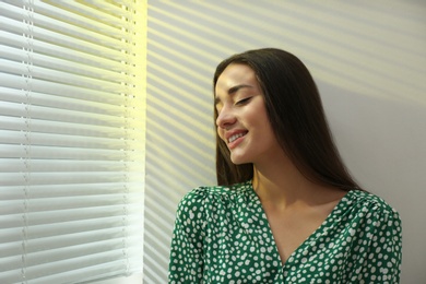 Young woman near window with Venetian blinds. Space for text