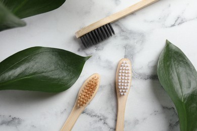 Bamboo toothbrushes and green leaves on white marble table, flat lay