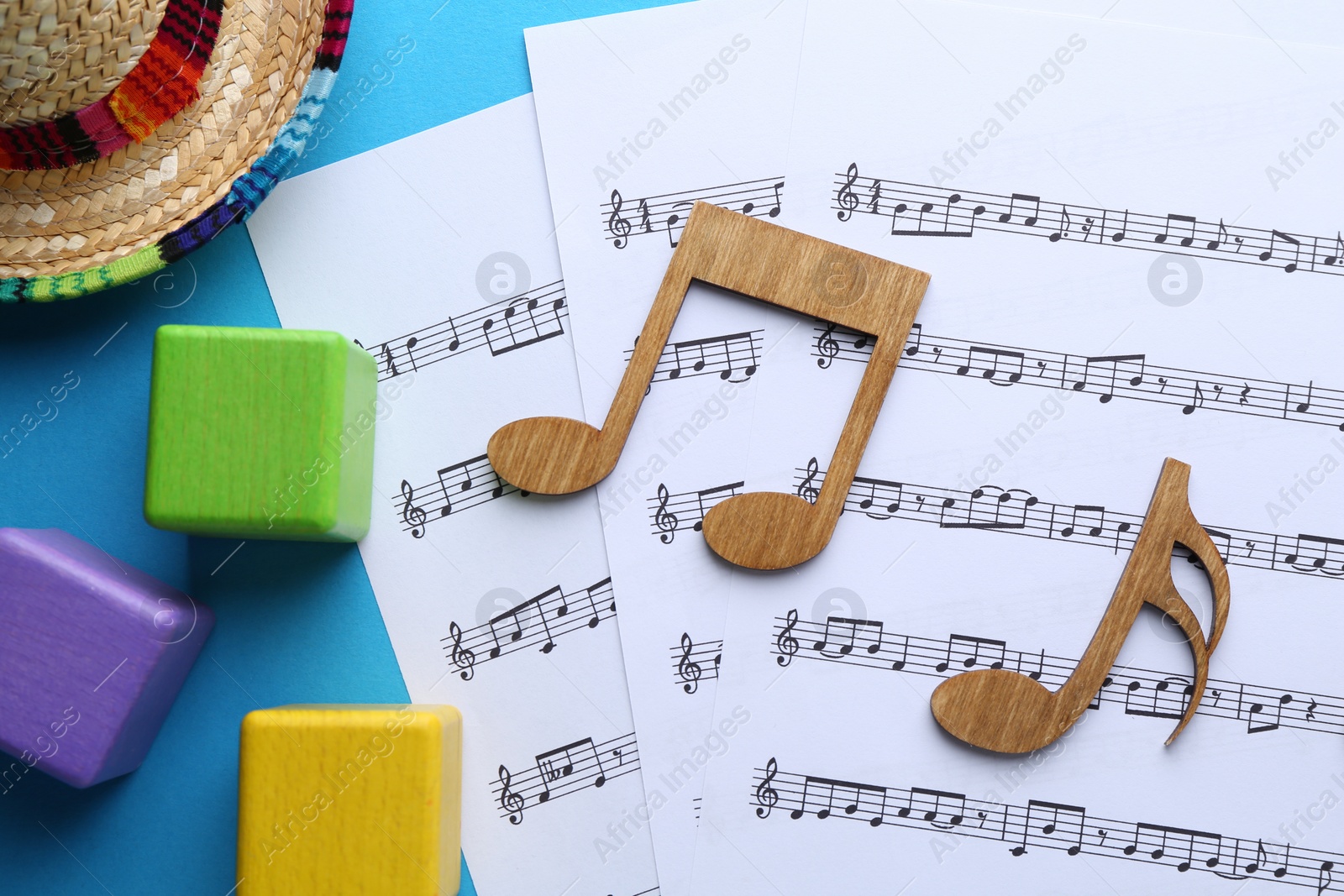 Photo of Baby songs. Music sheets, wooden notes, cubes and hat on light blue background, flat lay