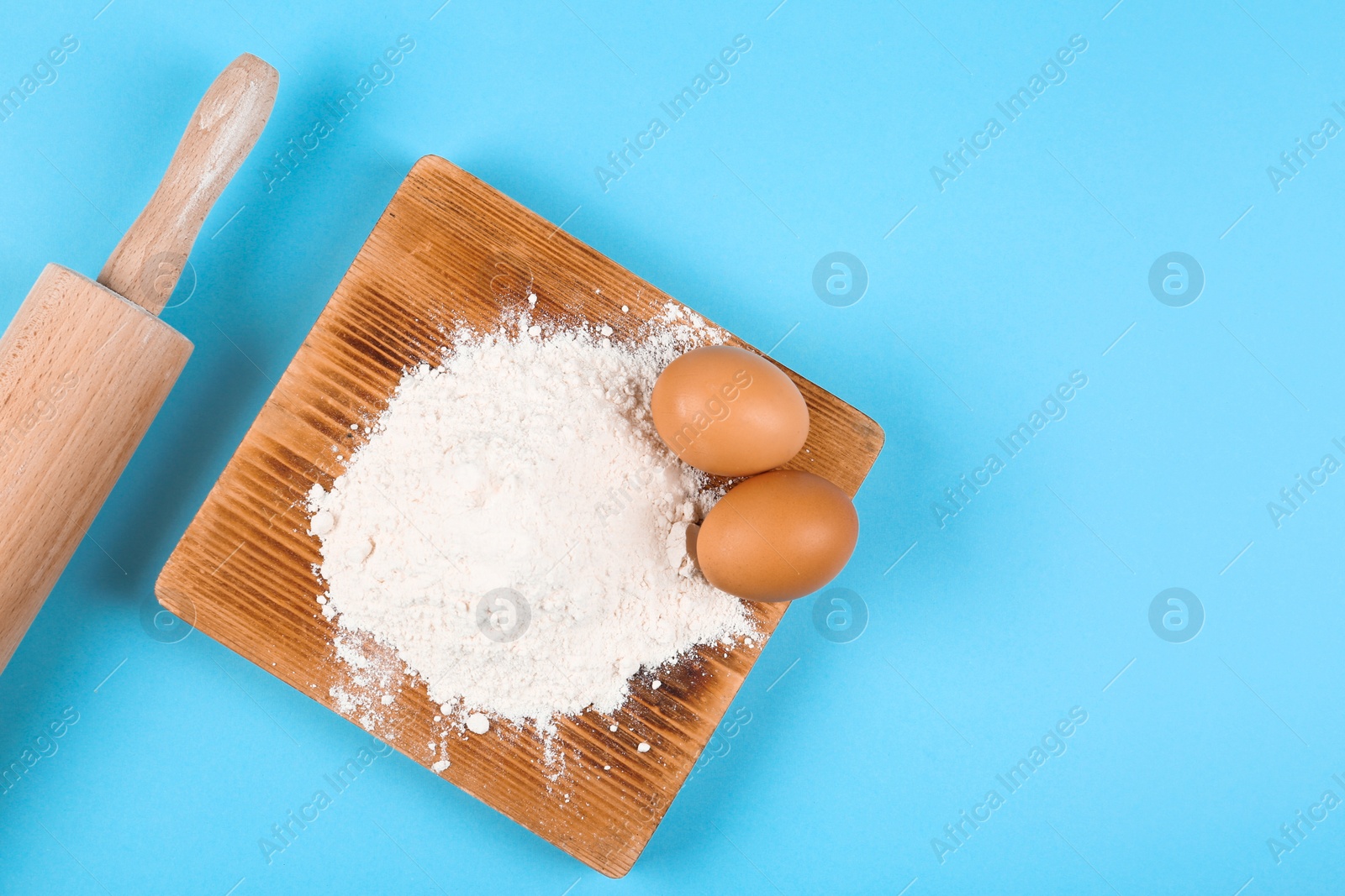 Photo of Raw eggs, rolling pin and flour on light blue background, flat lay. Baking pie