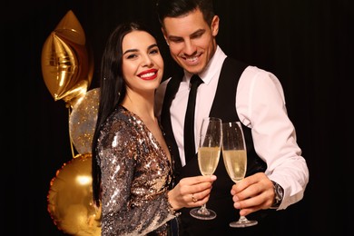 Photo of Happy couple with glasses of sparkling wine celebrating New Year on black background