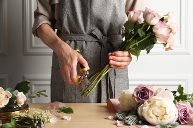 Photo of Florist cutting flower stems with pruner at workplace, closeup