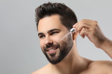 Photo of Handsome man applying cosmetic serum onto face on light grey background, closeup. Space for text