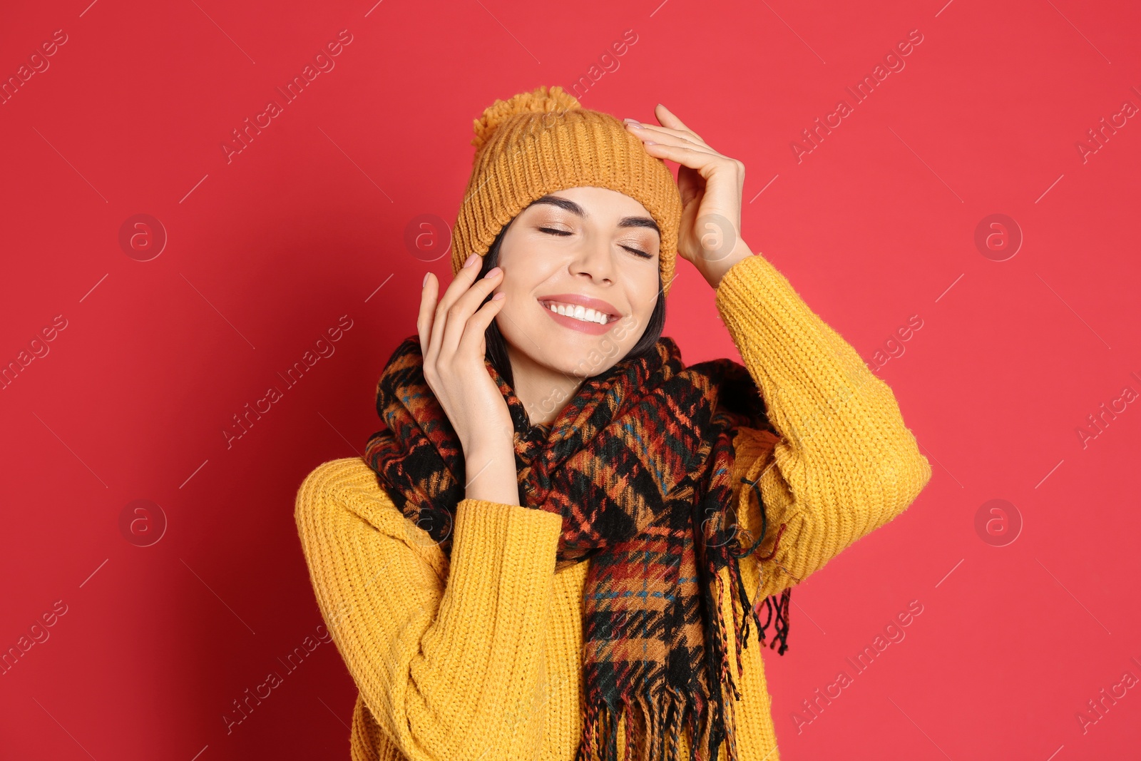 Photo of Young woman wearing warm sweater, scarf and hat on red background. Winter season