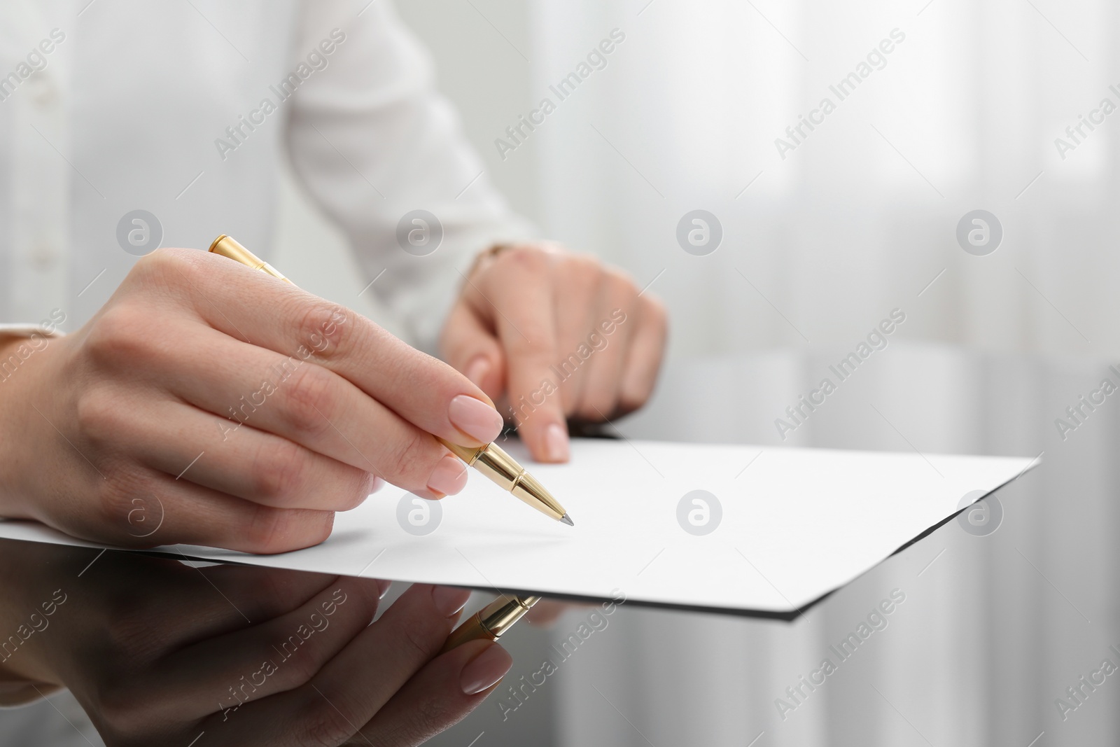 Photo of Woman writing on sheet of paper at glass table, closeup