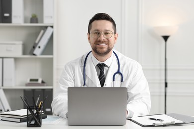 Photo of Smiling doctor with laptop at table in clinic. Online consultation