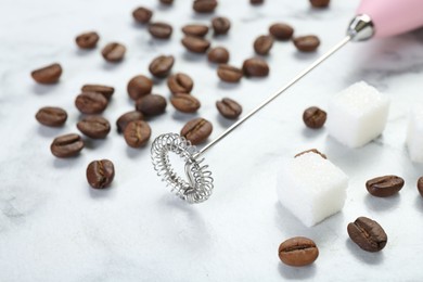 Photo of Pink milk frother wand, sugar cubes and coffee beans on white marble table, closeup