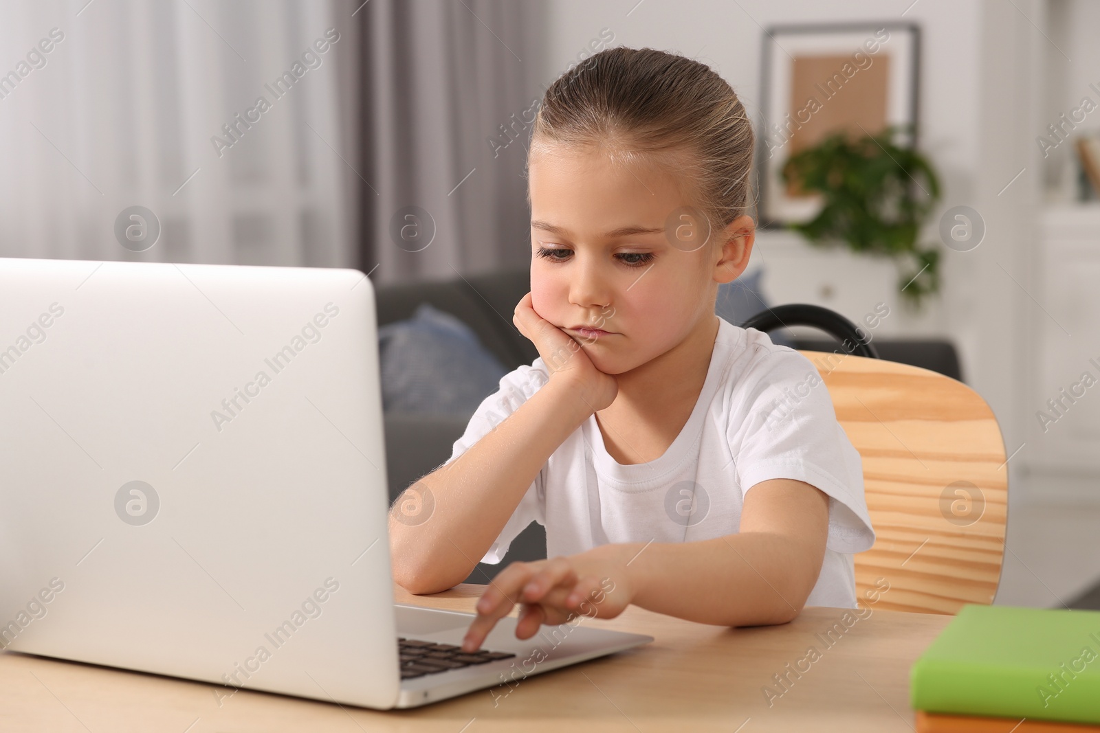 Photo of Little girl using laptop at table indoors. Internet addiction