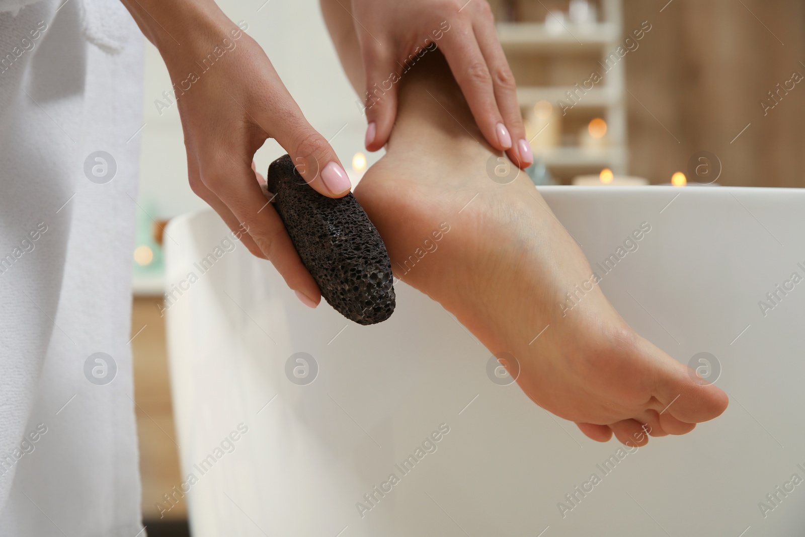 Photo of Woman using pumice stone for removing dead skin from feet in bathroom, closeup