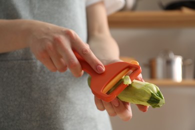 Photo of Woman peeling fresh zucchini indoors, closeup view