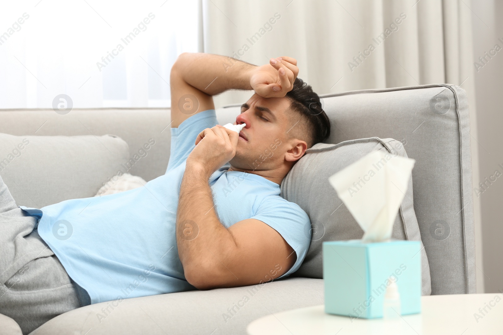 Photo of Ill man using nasal spray on sofa at home