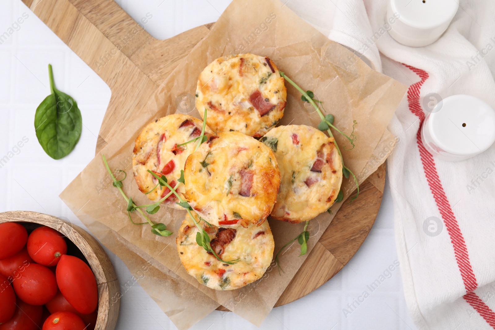 Photo of Delicious egg muffins with cheese and bacon on white tiled table, flat lay