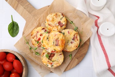 Photo of Delicious egg muffins with cheese and bacon on white tiled table, flat lay