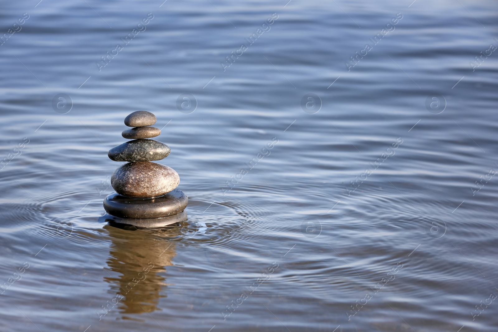 Photo of Stack of dark stones in sea water, space for text. Zen concept