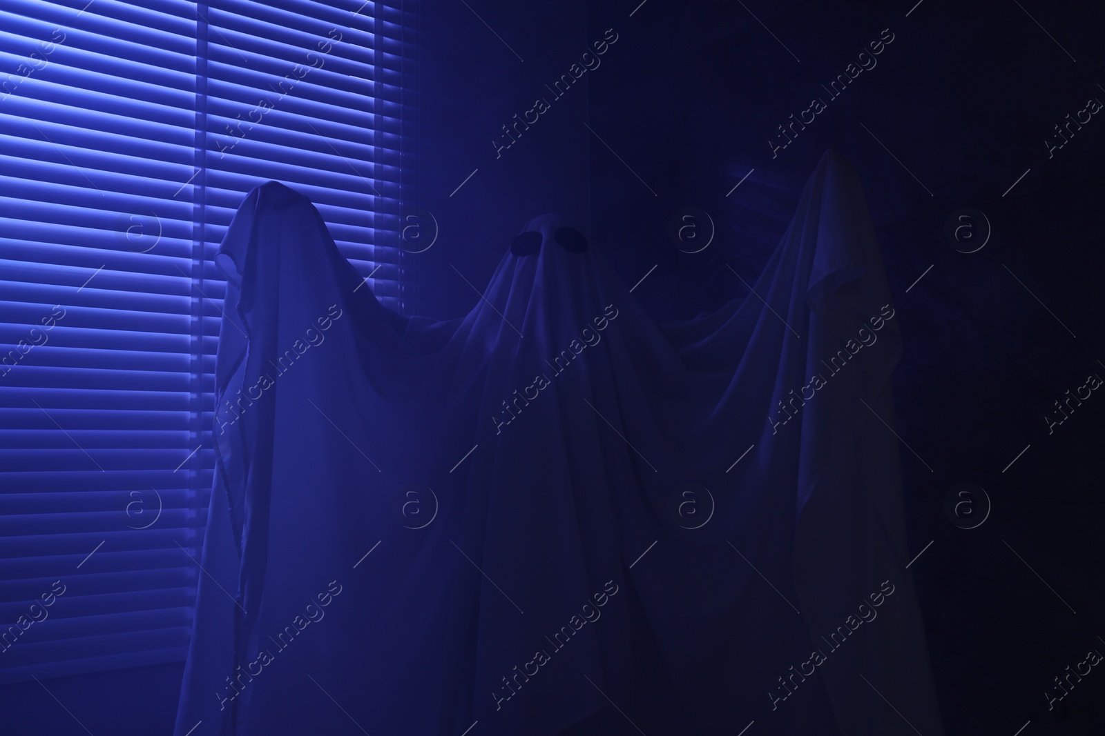 Photo of Creepy ghost. Woman covered with sheet near window in blue light