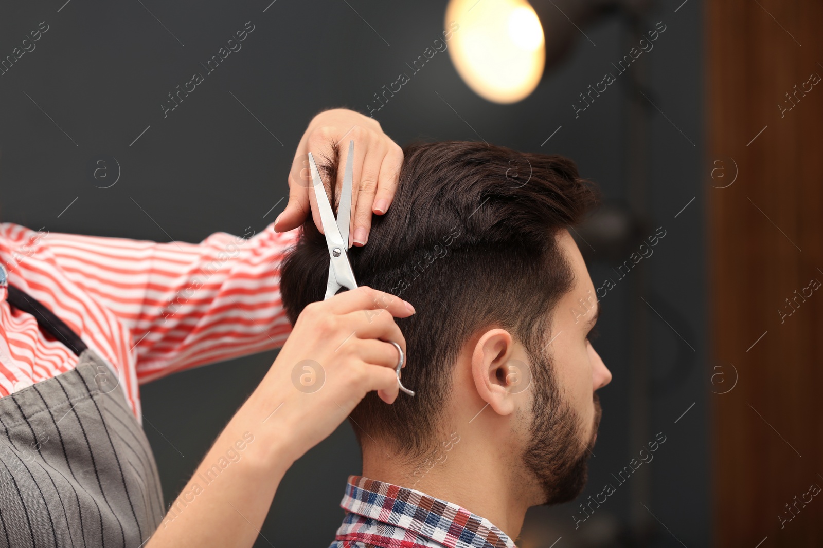 Photo of Barber making stylish haircut with professional scissors in beauty salon, closeup