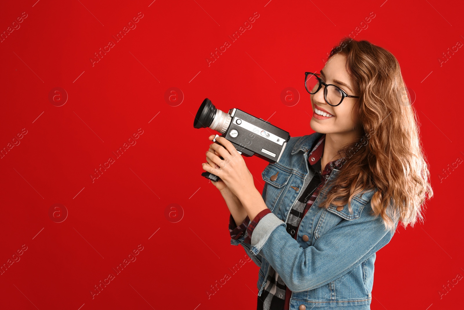 Photo of Beautiful young woman with vintage video camera on red background, space for text