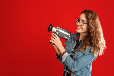 Beautiful young woman with vintage video camera on red background, space for text