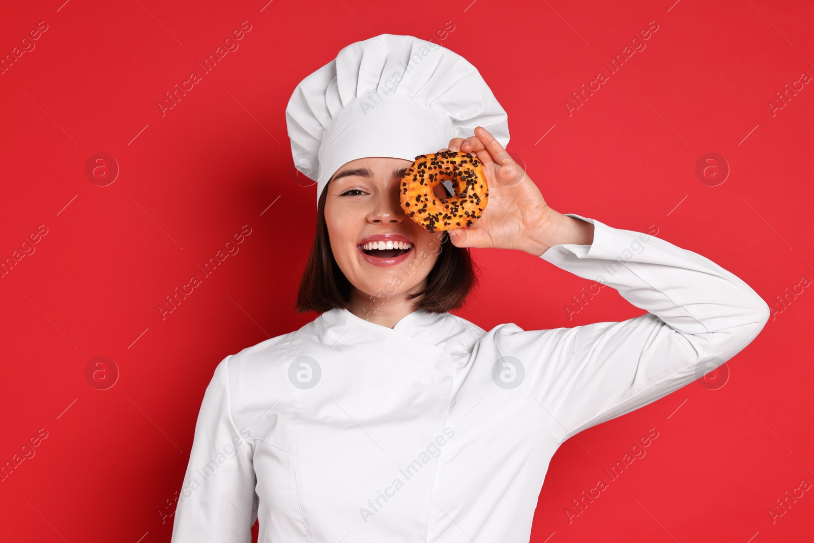 Photo of Happy confectioner with delicious donut on red background