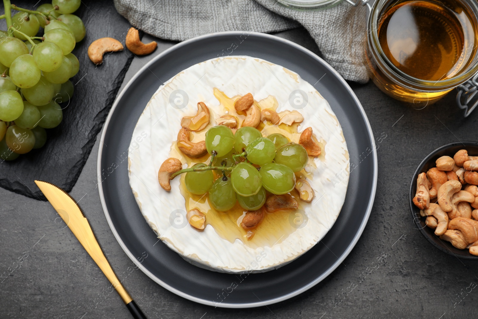 Photo of Brie cheese served with grape, cashew nuts and honey on dark grey table, flat lay