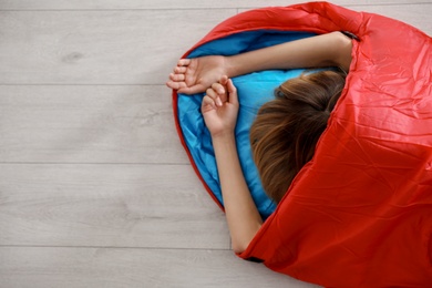 Photo of Young woman in comfortable sleeping bag on floor, top view. Space for text
