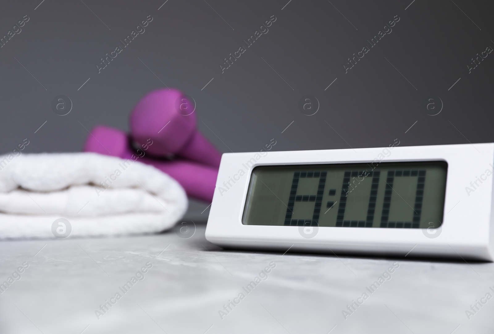 Photo of Alarm clock, dumbbells and towel on table against grey background, space for text. Morning exercise