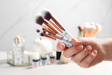Photo of Woman holding set of makeup brushes on blurred background, closeup