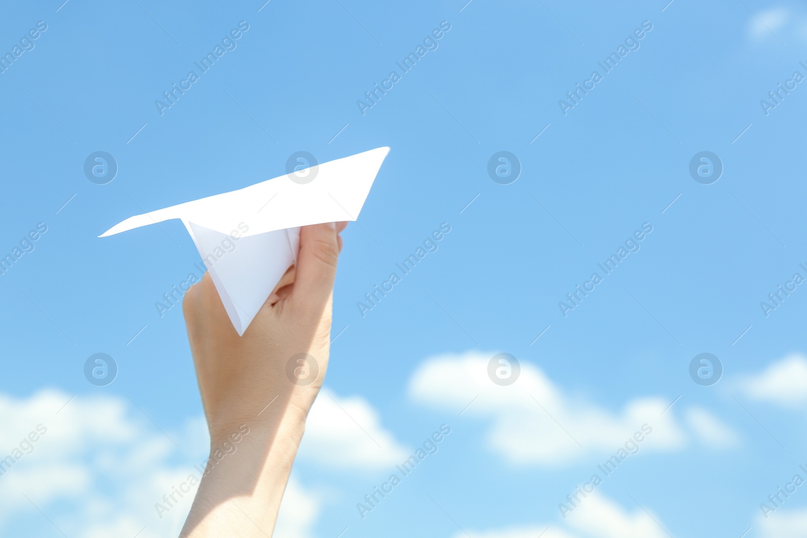 Photo of Woman holding paper plane against blue sky, closeup. Space for text