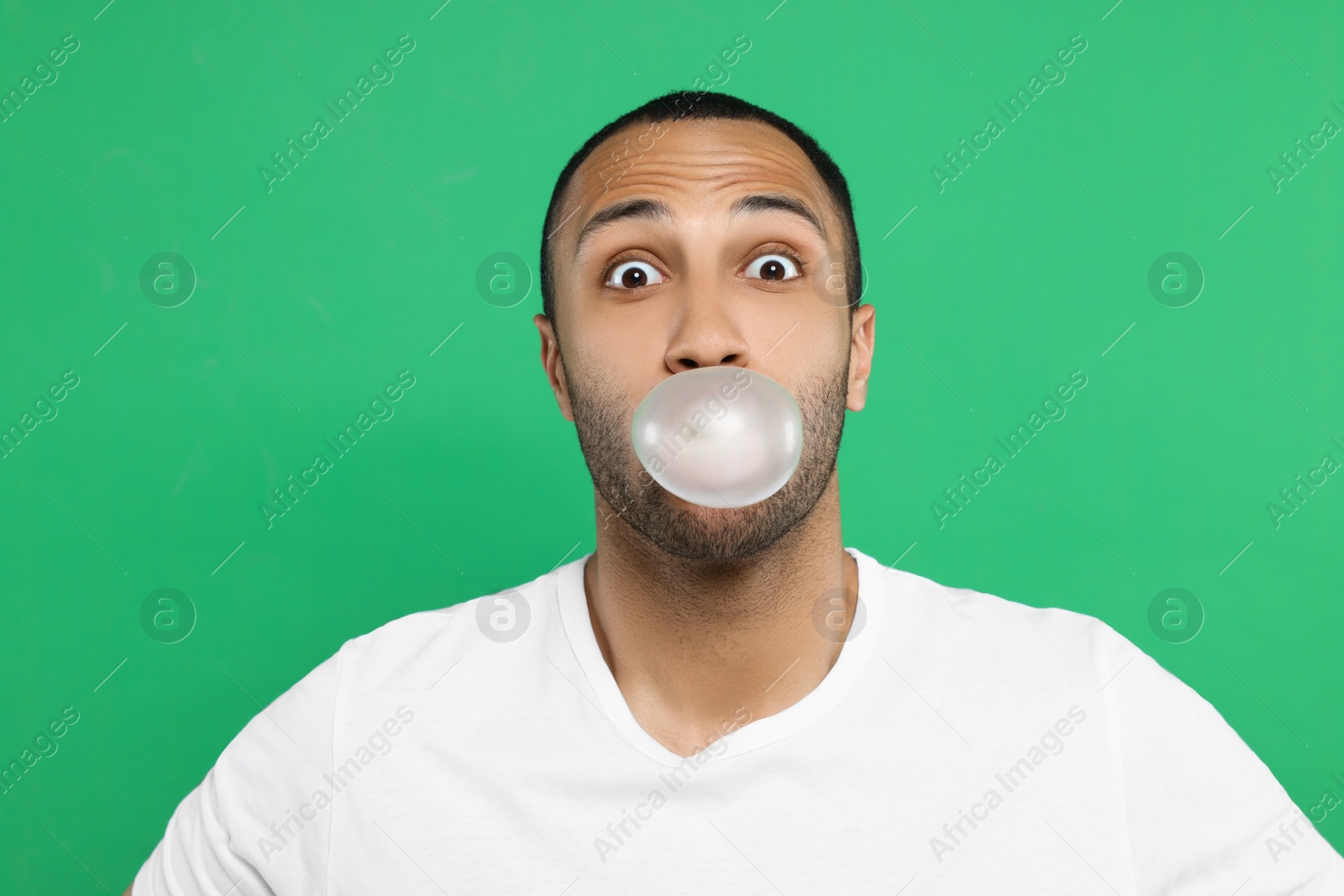 Photo of Portrait of young man blowing bubble gum on green background