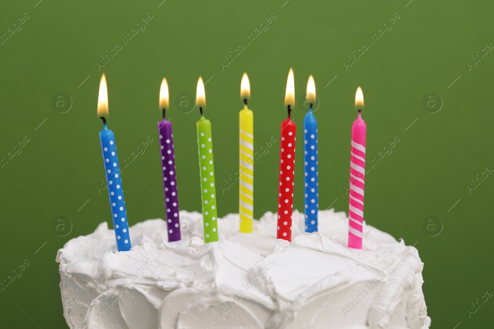 Photo of Delicious cake with cream and burning candles on green background, closeup