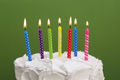 Delicious cake with cream and burning candles on green background, closeup