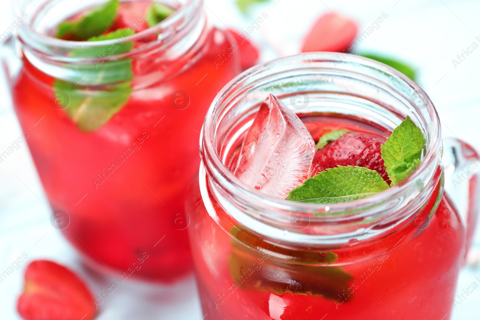 Photo of Mason jars of strawberry refreshing drink with ice cubes and mint on table, closeup