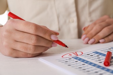 Photo of School grade. Teacher writing letter A with plus symbol on answer sheet at white table, closeup