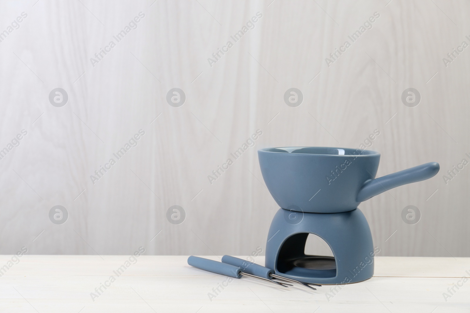 Photo of Fondue set on white wooden table, space for text