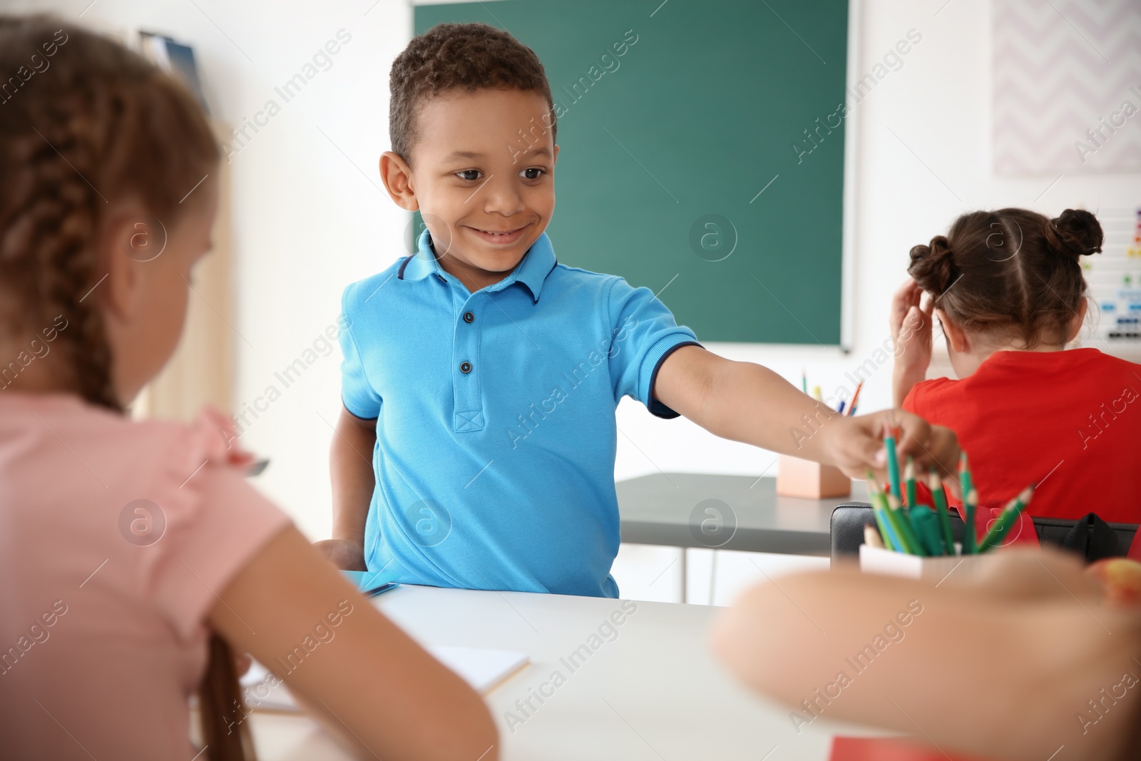 Photo of Cute little child taking his classmate's pencil at school