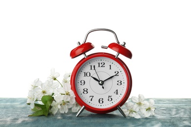 Photo of Alarm clock and branch with spring blossoms on wooden table against white background. Time change concept