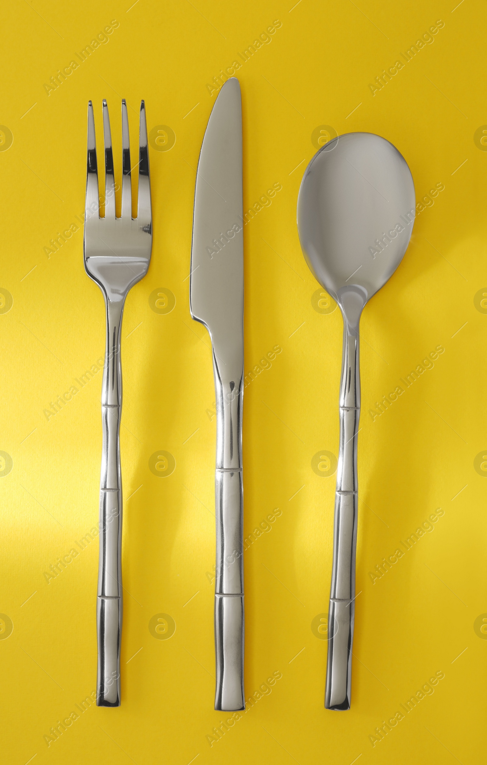 Photo of Spoon, fork and knife on yellow background, flat lay