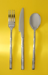 Spoon, fork and knife on yellow background, flat lay