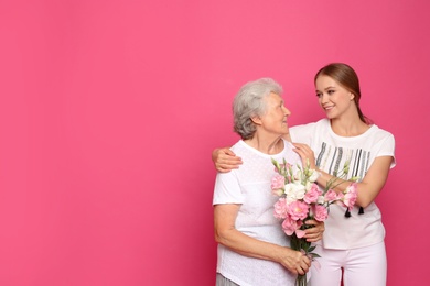 Photo of Young woman and her grandmother with flowers on pink background. Space for text