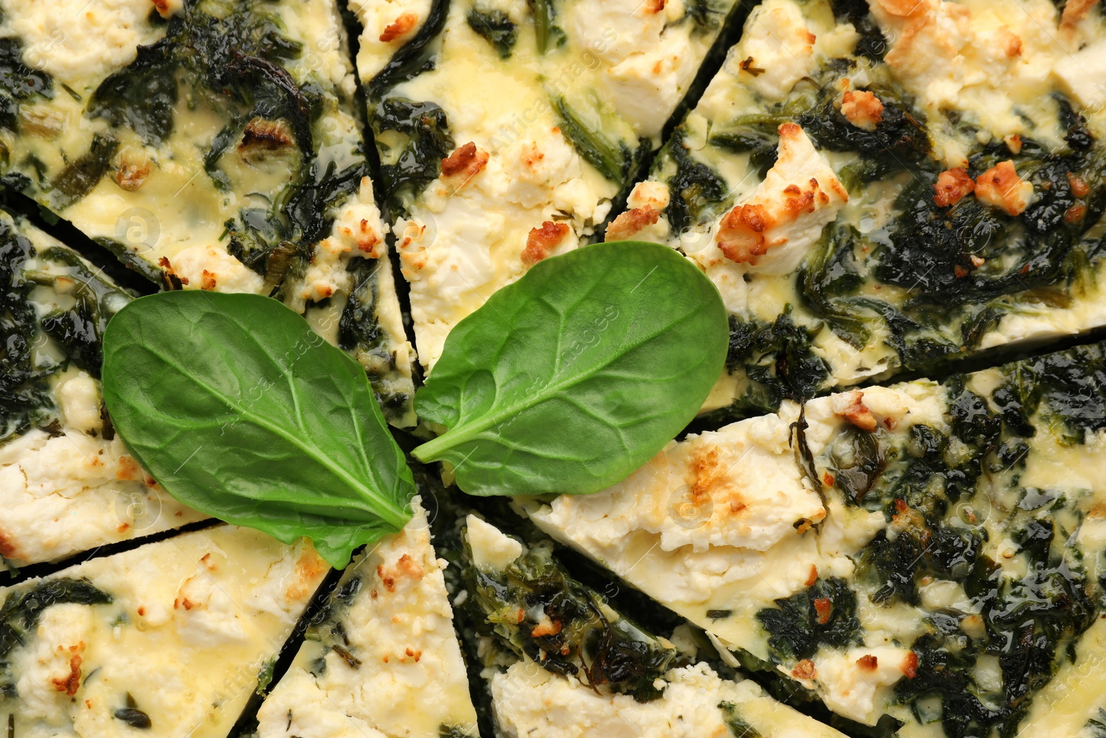 Photo of Delicious homemade spinach quiche and fresh leaves as background, closeup