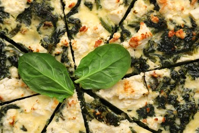 Delicious homemade spinach quiche and fresh leaves as background, closeup