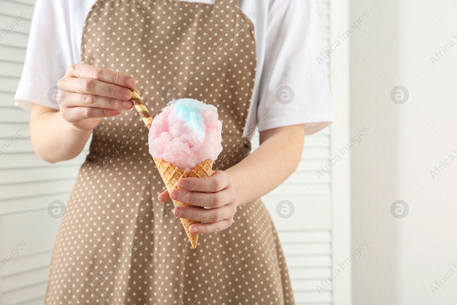 Photo of Woman holding waffle cone with cotton candy indoors, closeup