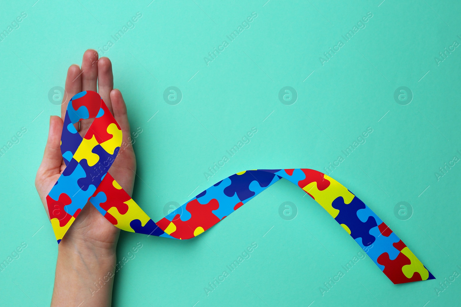 Image of World Autism Awareness Day. Woman with colorful puzzle ribbon on cyan background, top view