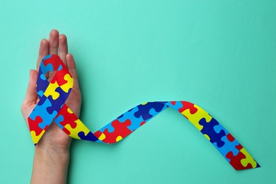 World Autism Awareness Day. Woman with colorful puzzle ribbon on cyan background, top view