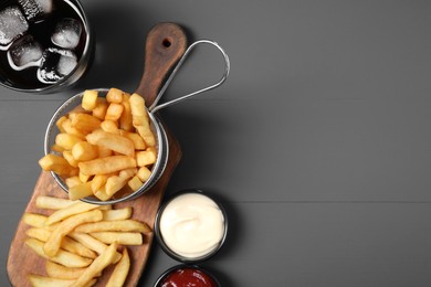 Photo of Tasty French fries, soda, ketchup and mayonnaise on grey table, flat lay. Space for text
