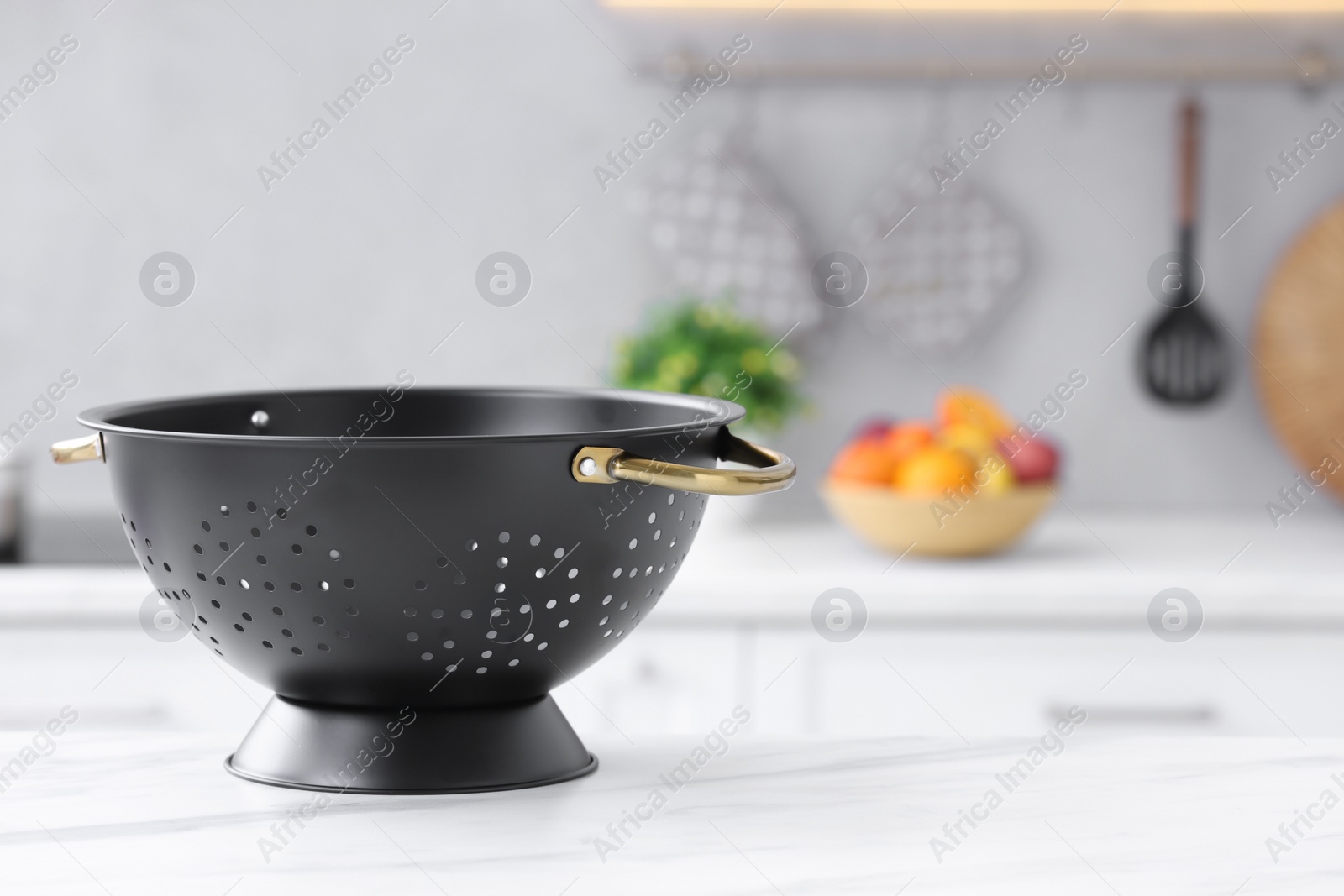 Photo of Black colander on white marble table in kitchen. Space for text