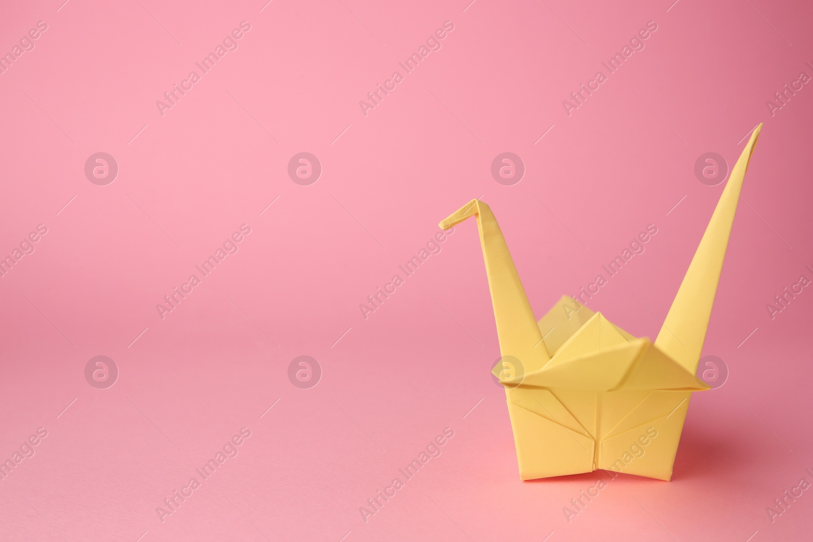 Photo of Origami art. Handmade paper crane on pink background, space for text